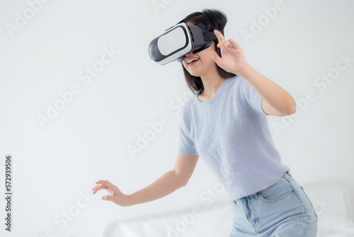 Young asian woman wearing vr headset playing game with excited in the bedroom at home, female using virtual reality or metaverse innovation for simulation 3D, lifestyles and technology concept.
