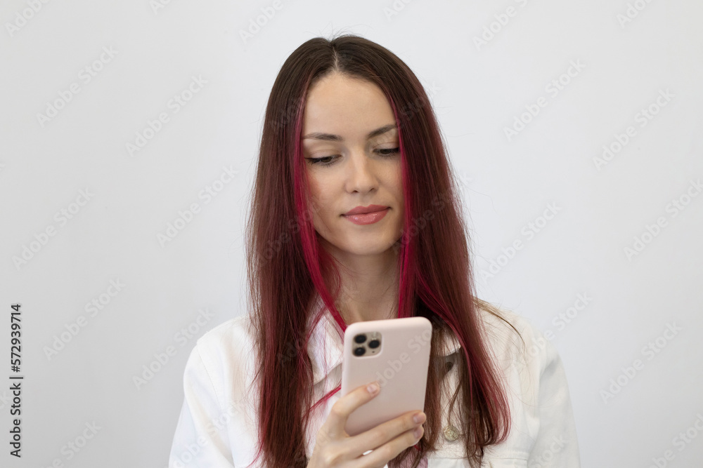 Portrait of a bright, beautiful young woman with pink hair looking into her phone. The girl on a white background. Portrait of a bright, beautiful young woman with pink hair looking into her phone. The girl on a white background.