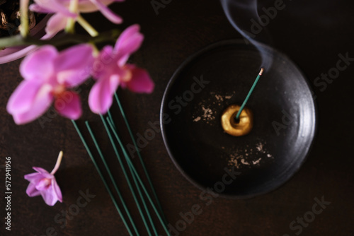 Overhead view of burning japanese incense stick with smoke on round black holder and pink orchid flowers