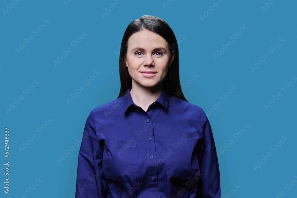 Fototapeta premium Smiling young woman looking at camera on blue background