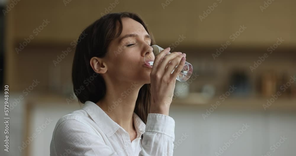 Peaceful thirsty young woman drinking fresh clean pure water from transparent glass, keeping hydration balance, healthy metabolism, opening closed eyes, looking away, smiling with satisfaction Peaceful thirsty young woman drinking fresh clean pure water from transparent glass, keeping hydration balance, healthy metabolism, opening closed eyes, looking away, smiling with satisfaction