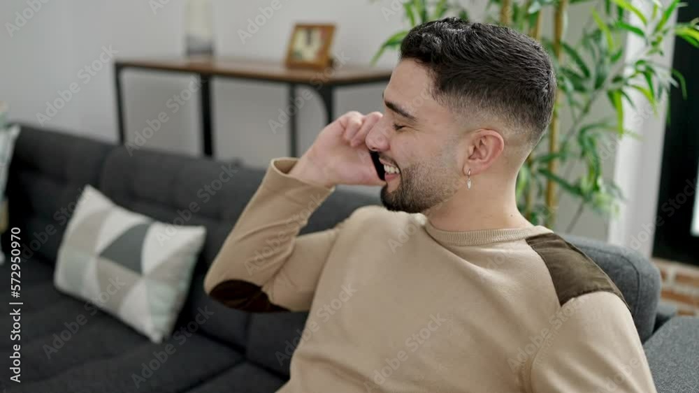 Young arab man talking on the smartphone sitting on sofa at home Young arab man talking on the smartphone sitting on sofa at home