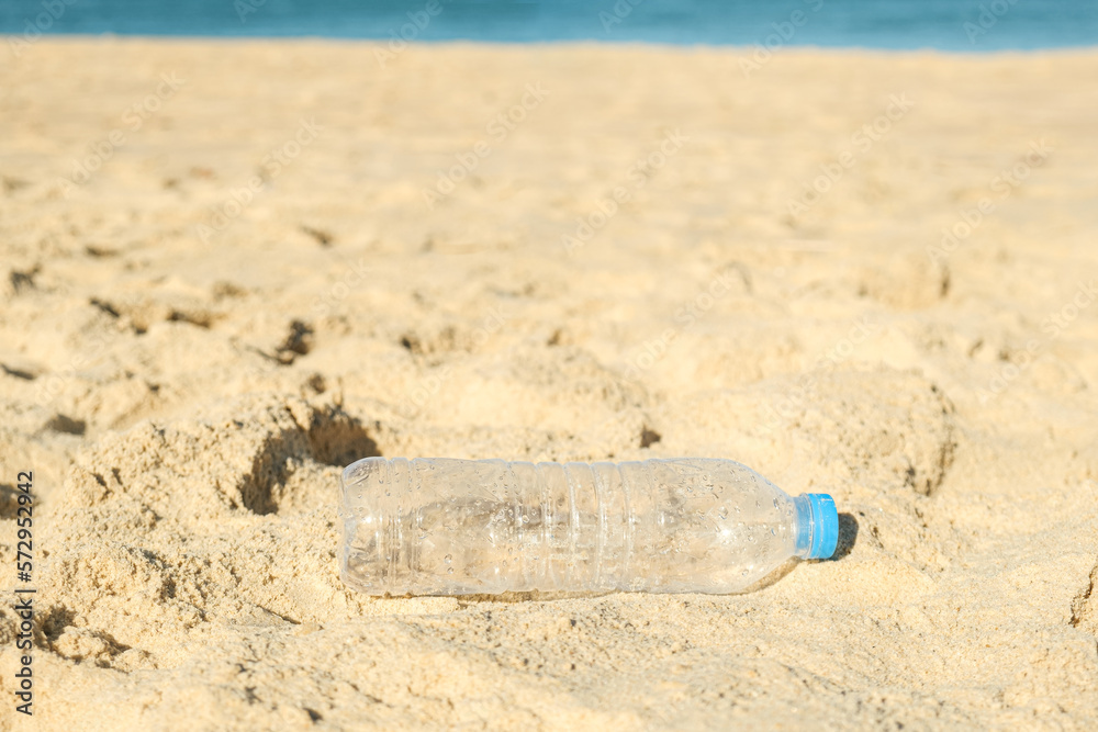 Empty plastic bottle from drinking water lying on the sandy beach. The problem of ocean plastic pollution. Ecological problem, used plastic bottle on sea shore Empty plastic bottle from drinking water lying on the sandy beach. The problem of ocean plastic pollution. Ecological problem, used plastic bottle on sea shore