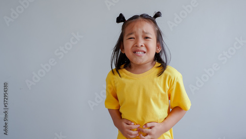 Studio portrait of sick child girl touches herself stomach and looks unhappy.

