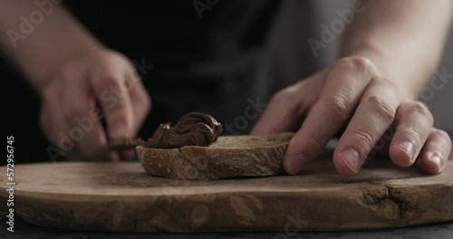 man spreading chocolate hazelnut spread on ciabatta slice on wood board