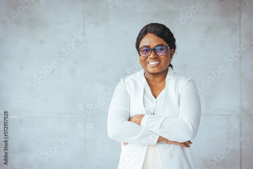 Studio portrait of happy successful confident black business woman. Beautiful young lady in white jacket smiling at camera standing isolated on blank solid gray colour copyspace background