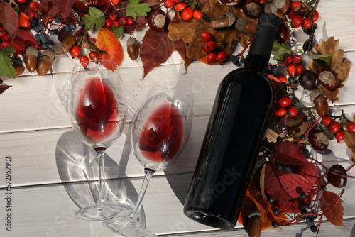 glass of red wine on wooden background with autumn leaves and bottle 