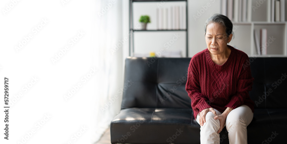 Fototapeta premium Senior woman suffering from pain in knee in the living room at her home.