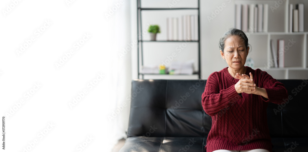 Asian woman hand suffering from joint pain, trying to message her finger while sitting on the sofa. Asian woman hand suffering from joint pain, trying to message her finger while sitting on the sofa.
