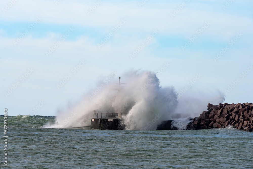 Massive wave hits a small lighthouse on a jetty