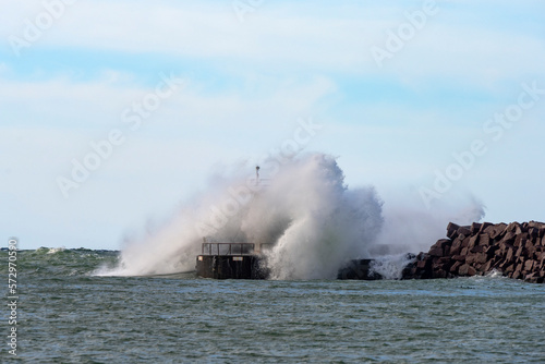 Massive wave hits a small lighthouse on a jetty