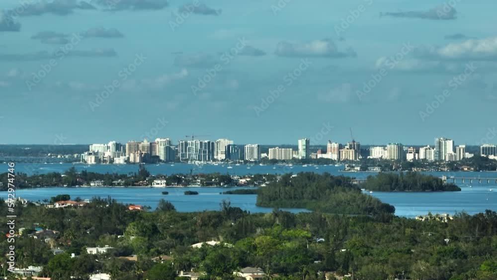 Aerial view of distant downtown of Sarasota city in Florida, USA with high skyscrapers and office buildings on horizon and green suburbs in front Aerial view of distant downtown of Sarasota city in Florida, USA with high skyscrapers and office buildings on horizon and green suburbs in front