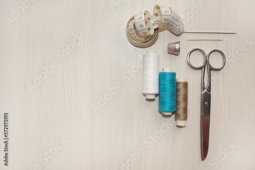 Sewing accessories, threads, needles, scissors, thimble on a white table. Sewing and hobby concept.