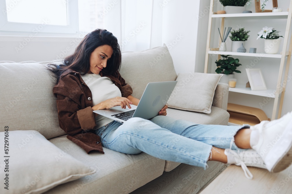 Woman freelancer on day off sitting on sofa with laptop at home online shopping on internet, smile Woman freelancer on day off sitting on sofa with laptop at home online shopping on internet, smile