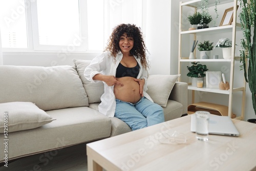 Pregnant woman smile and happiness sits on the couch freedom and strokes her belly feels kicks with the baby in the last month of pregnancy, mother's day lifestyle