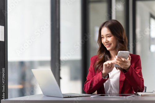 business woman holding smartphone getting message with confirmation making transaction on laptop computer at office