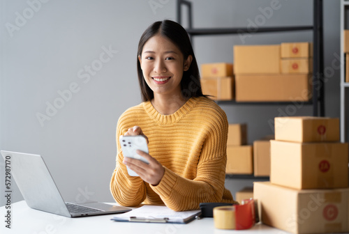 Young Adorable Asian online business owner using her smartphone to gather more information while sitting in her room.