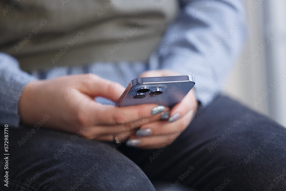 Young woman holding smart phone and browsing app. Close up photo of modern blue mobile phone in female hands Young woman holding smart phone and browsing app. Close up photo of modern blue mobile phone in female hands