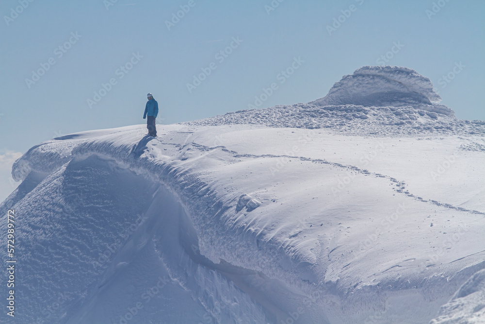 Mountaineer reaches the top of a snowy mountain in a sunny winter day.