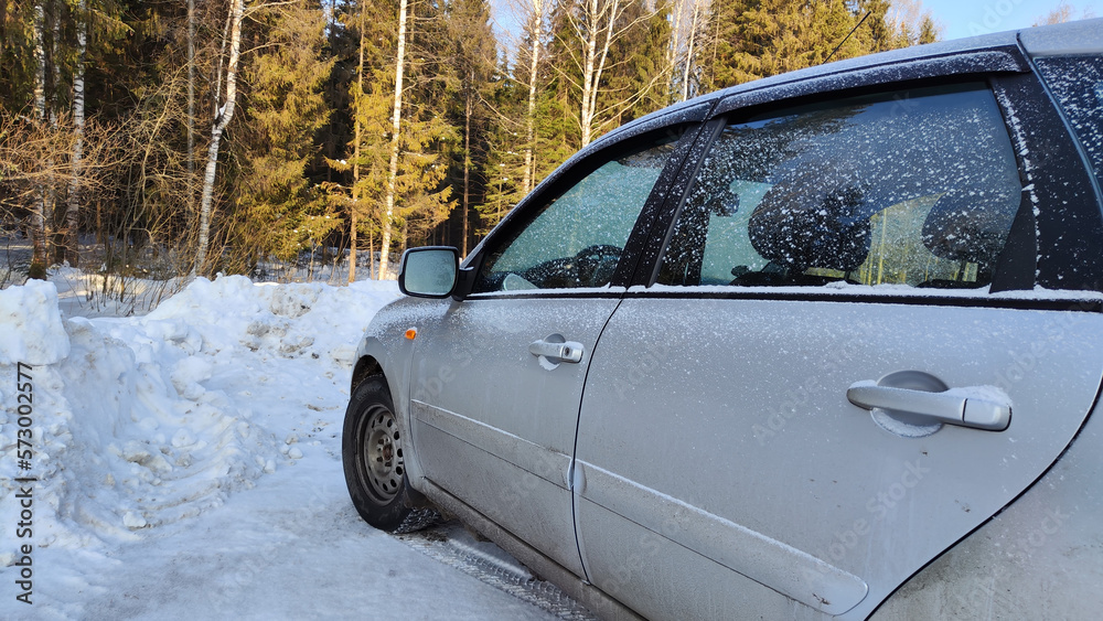 Obraz premium The side of a car standing in the snow near the forest on a winter day