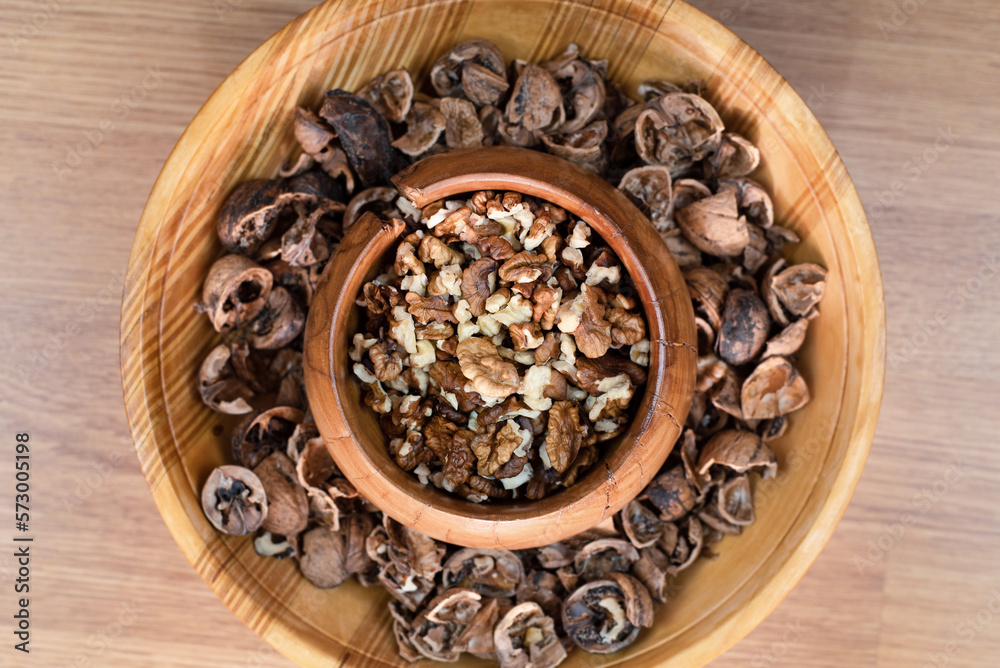 An authentic wooden plate has walnuts and another plate has a walnut shell next to it, top view, selective focus An authentic wooden plate has walnuts and another plate has a walnut shell next to it, top view, selective focus
