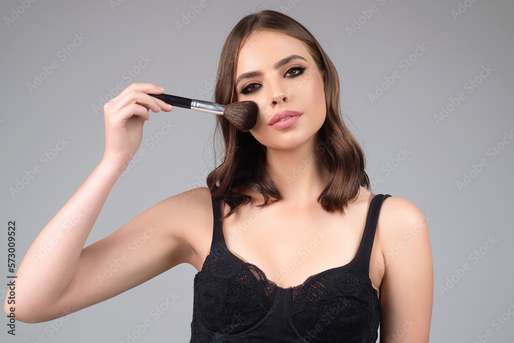Obraz premium Woman applying foundation powder or blush with makeup brush. Facial treatment, perfect skin, natural make up, facial beauty. Isolated on studio background. Applying makeup.