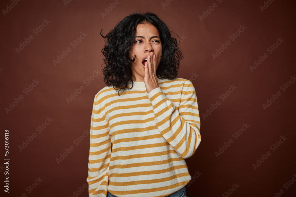 Young colombian curly hair woman isolated on brown background yawning showing a tired gesture covering mouth with hand. Young colombian curly hair woman isolated on brown background yawning showing a tired gesture covering mouth with hand.
