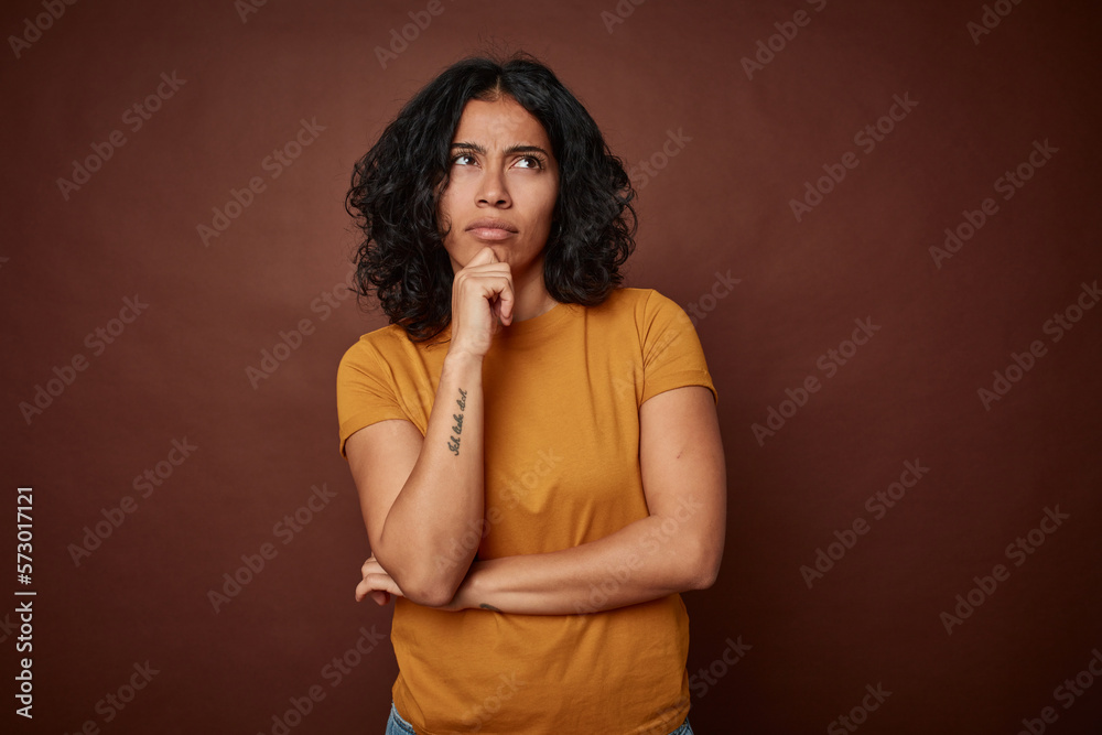 Young colombian curly hair woman isolated on brown background looking sideways with doubtful and skeptical expression. Young colombian curly hair woman isolated on brown background looking sideways with doubtful and skeptical expression.
