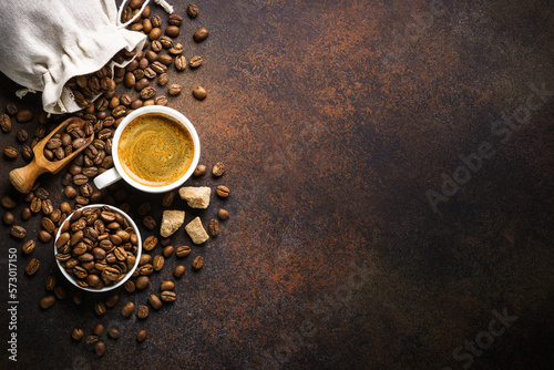 Cup of coffee, roasted coffee beans and sugar at dark table . Top view image with copy space.