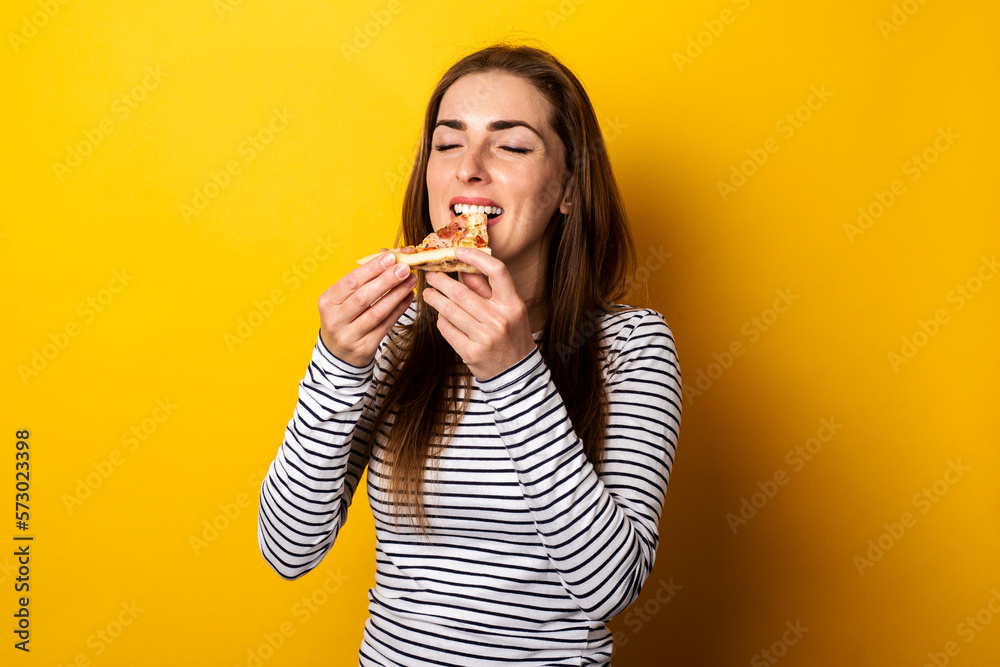 young woman with closed eyes eating a slice of hot fresh pizza on a yellow background young woman with closed eyes eating a slice of hot fresh pizza on a yellow background