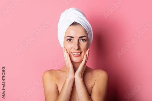 smiling young woman with towel on head, nude shoulders on pink background.