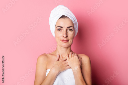 daily spa. Young woman with a towel on her head, head touching her soft skin on the neck on a pink background