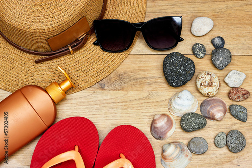 Summer concept, sun cream and slipper and stones, sunglasses and seashell on wood table