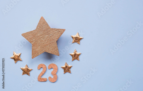 Greeting card for the Defender of the Fatherland Day. Gold stars and the number 23 on a light blue background. The holiday is February 23.