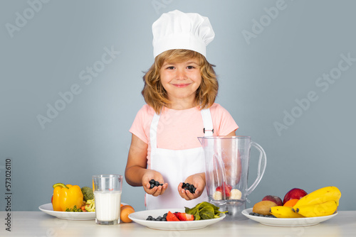 Portrait of chef child in cook hat cooking blueberries smoothie. Cooking at home, kid boy preparing food from vegetable and fruits. Healthy eating.