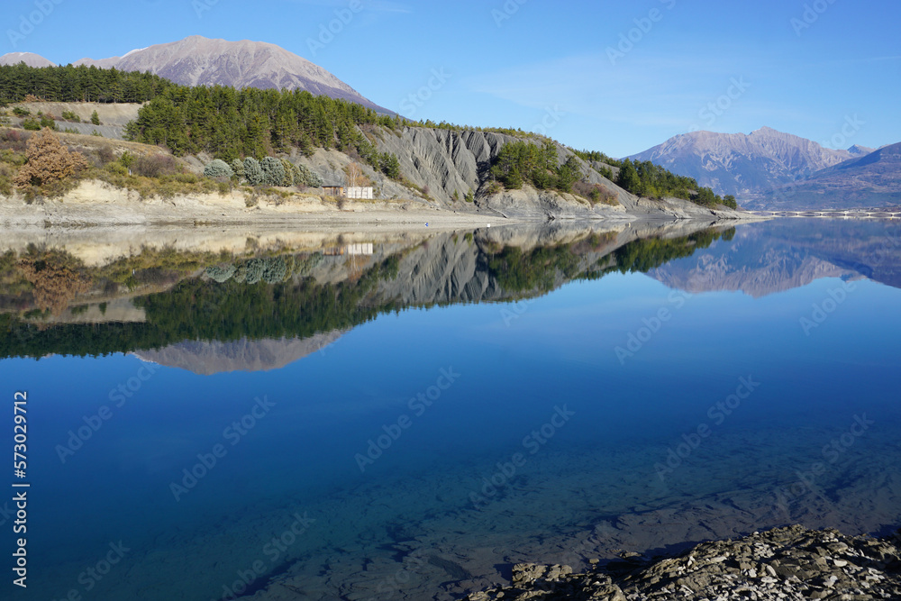 mirror reflection of the mountains in Serre Ponçon lake, Alps, France on a summer day