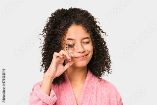 Young african american curly woman using an eyelash curler isolated