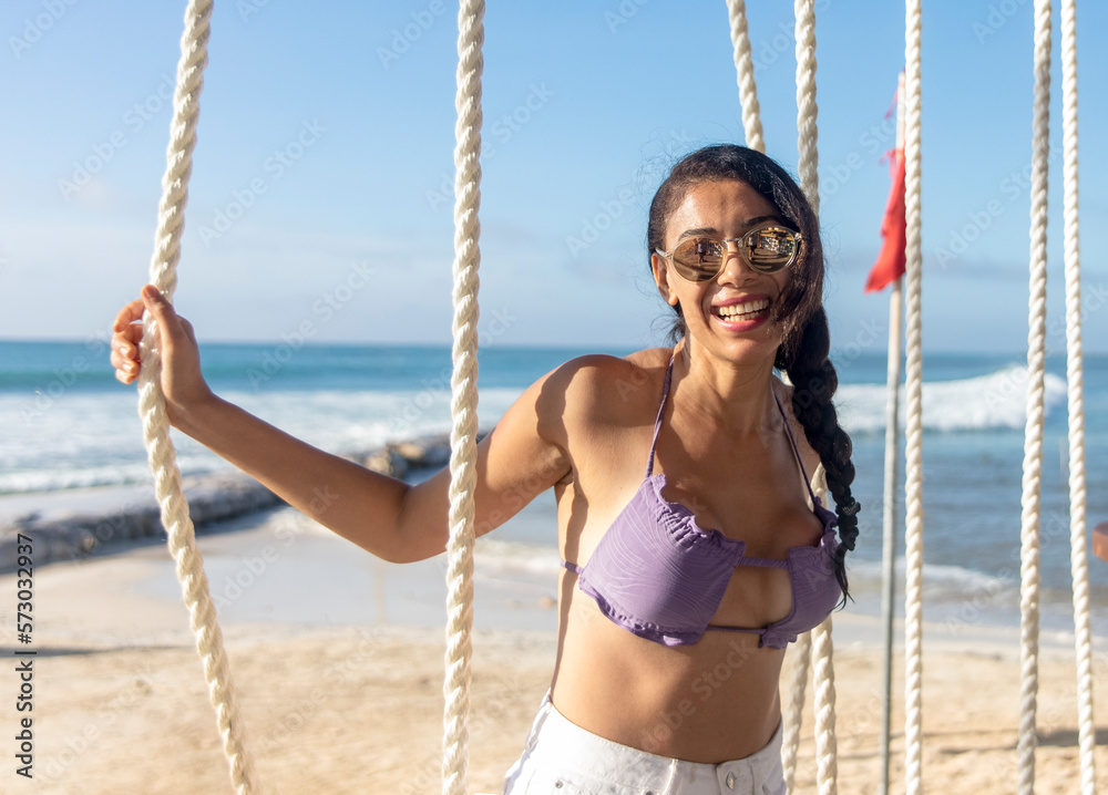 Young woman with sexy and beautiful smile attentive to the swing ropes in the Mexican Mayan Riviera, enjoying while swinging and contemplating a beautiful view of a beautiful white beach.