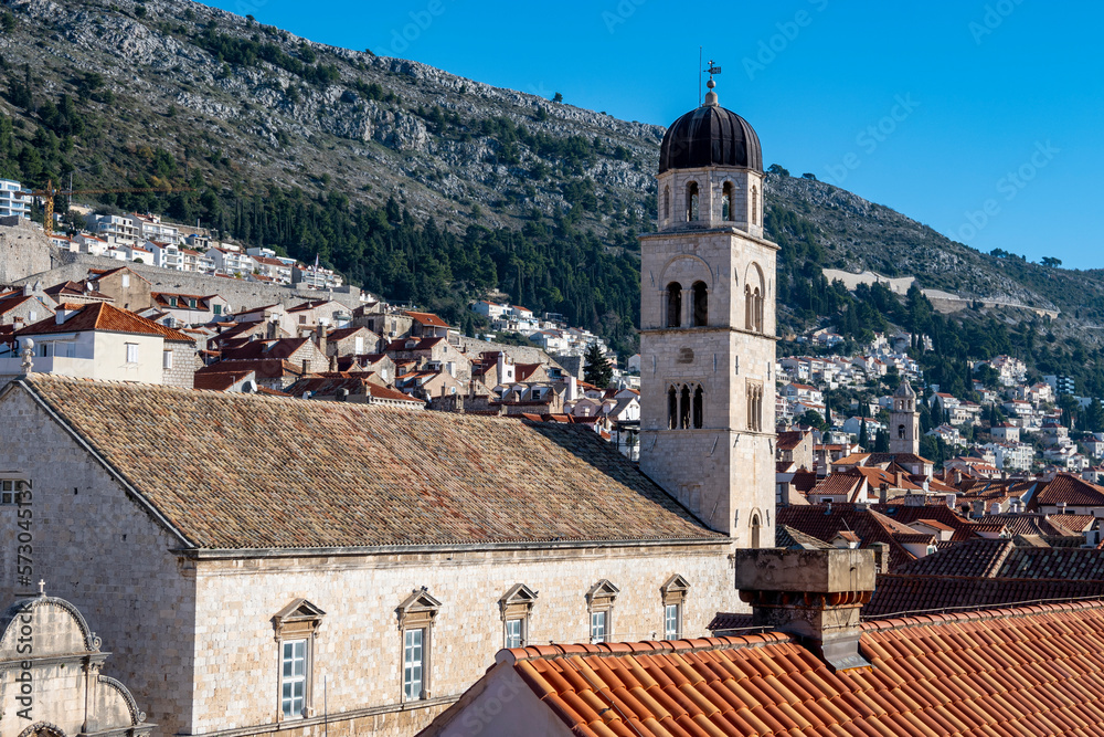 Franciscan Church and Monastery rising above Stradun street in amazing, fortified city of Dubrovnik, with rows of houses on the steep slopes in the background