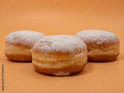 Freshly baked and dusted with powdered sugar German donuts. Donut berliner or krapfen on orange background.