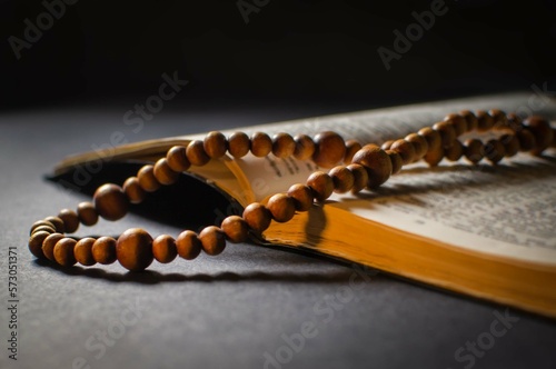 Close-up of an open Bible with blurred text and a wooden rosary on a black background with a golden glow. The concept of reading Christian literature. Selective focus, blur, low key.