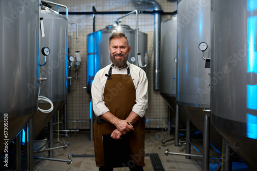 Portrait of smiling brewer man in apron standing among distillery vats
