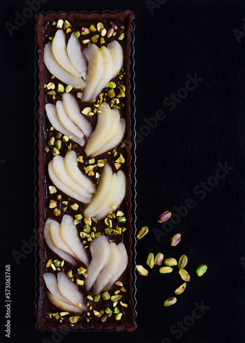 Tarta de chocolate, pera y pistachos sobre fondo negro, vista superior. Tarta fina alargada. 