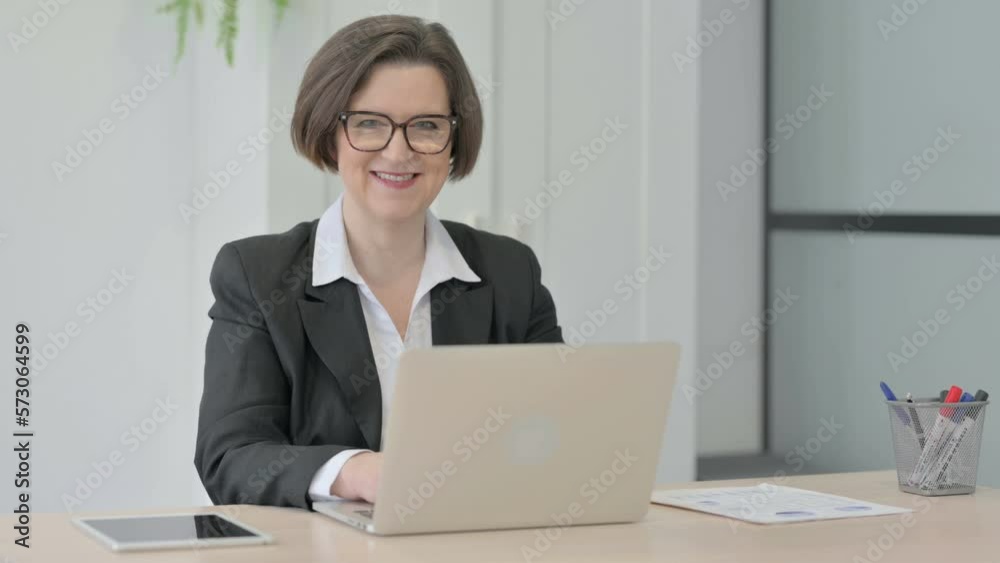 Old Businesswoman Smiling at Camera while using Laptop Old Businesswoman Smiling at Camera while using Laptop