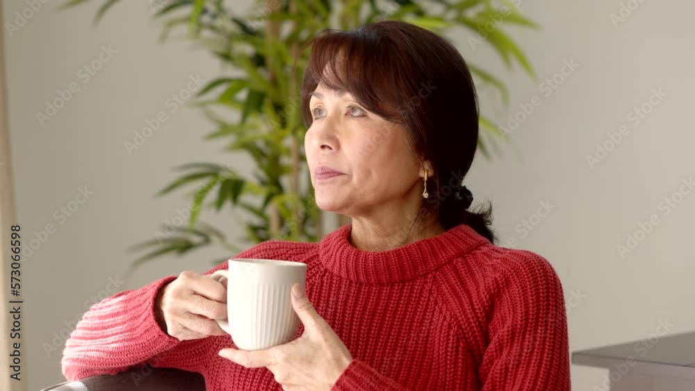 Attractive middle age woman red sweater enjoying drinking coffee looking out bright window sitting on home living room sofa indoor tree background Attractive middle age woman red sweater enjoying drinking coffee looking out bright window sitting on home living room sofa indoor tree background