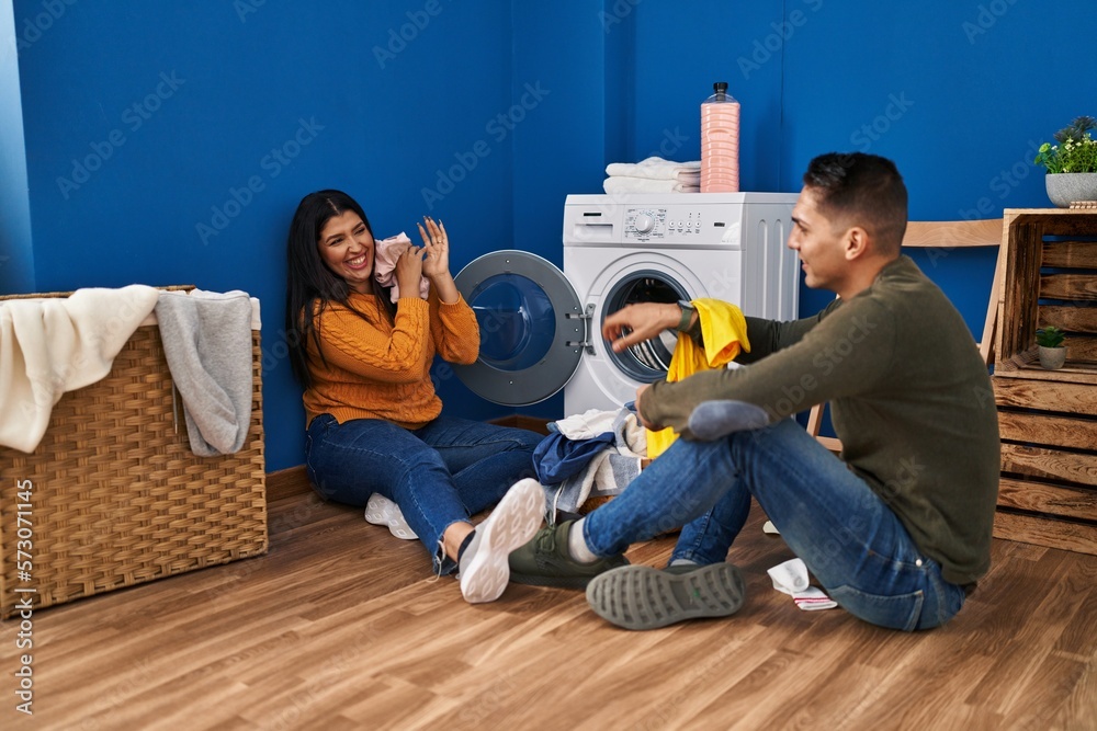 Man and woman couple smiling confident playing with clothes at laundry room Man and woman couple smiling confident playing with clothes at laundry room