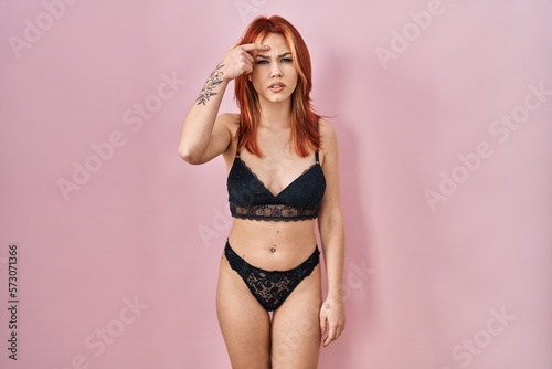 Young caucasian woman wearing lingerie over pink background pointing unhappy to pimple on forehead, ugly infection of blackhead. acne and skin problem © Krakenimages.com