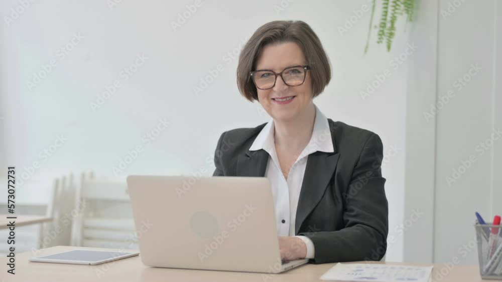 Old Businesswoman Smiling at Camera while using Laptop Old Businesswoman Smiling at Camera while using Laptop