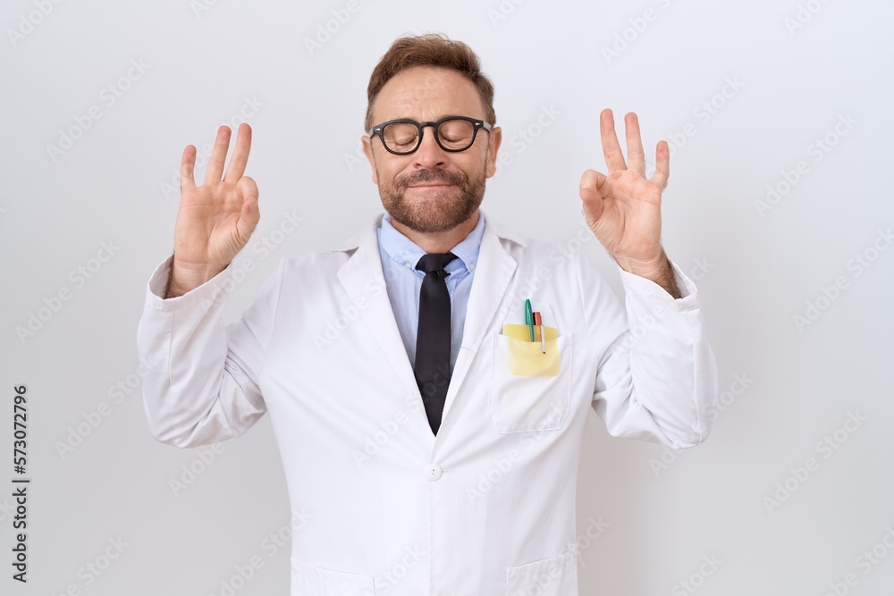 Middle age doctor man with beard wearing white coat relax and smiling with eyes closed doing meditation gesture with fingers. yoga concept. Middle age doctor man with beard wearing white coat relax and smiling with eyes closed doing meditation gesture with fingers. yoga concept.