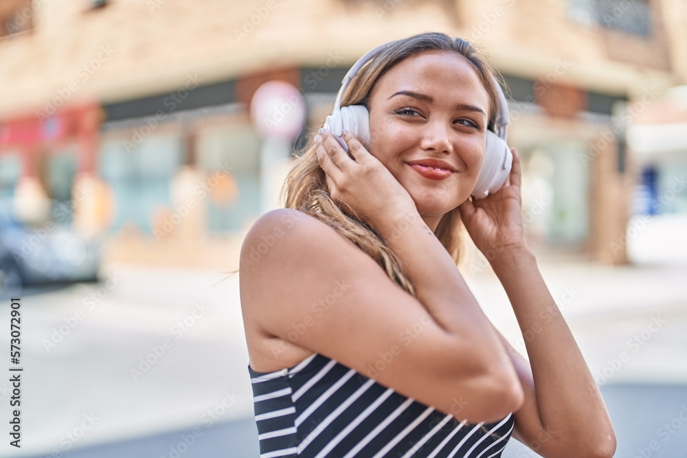 Young beautiful hispanic woman listening to music standing at street